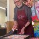 two people wearing aprons with one cutting food on a tray