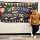 Teacher by a welcome back to school banner
